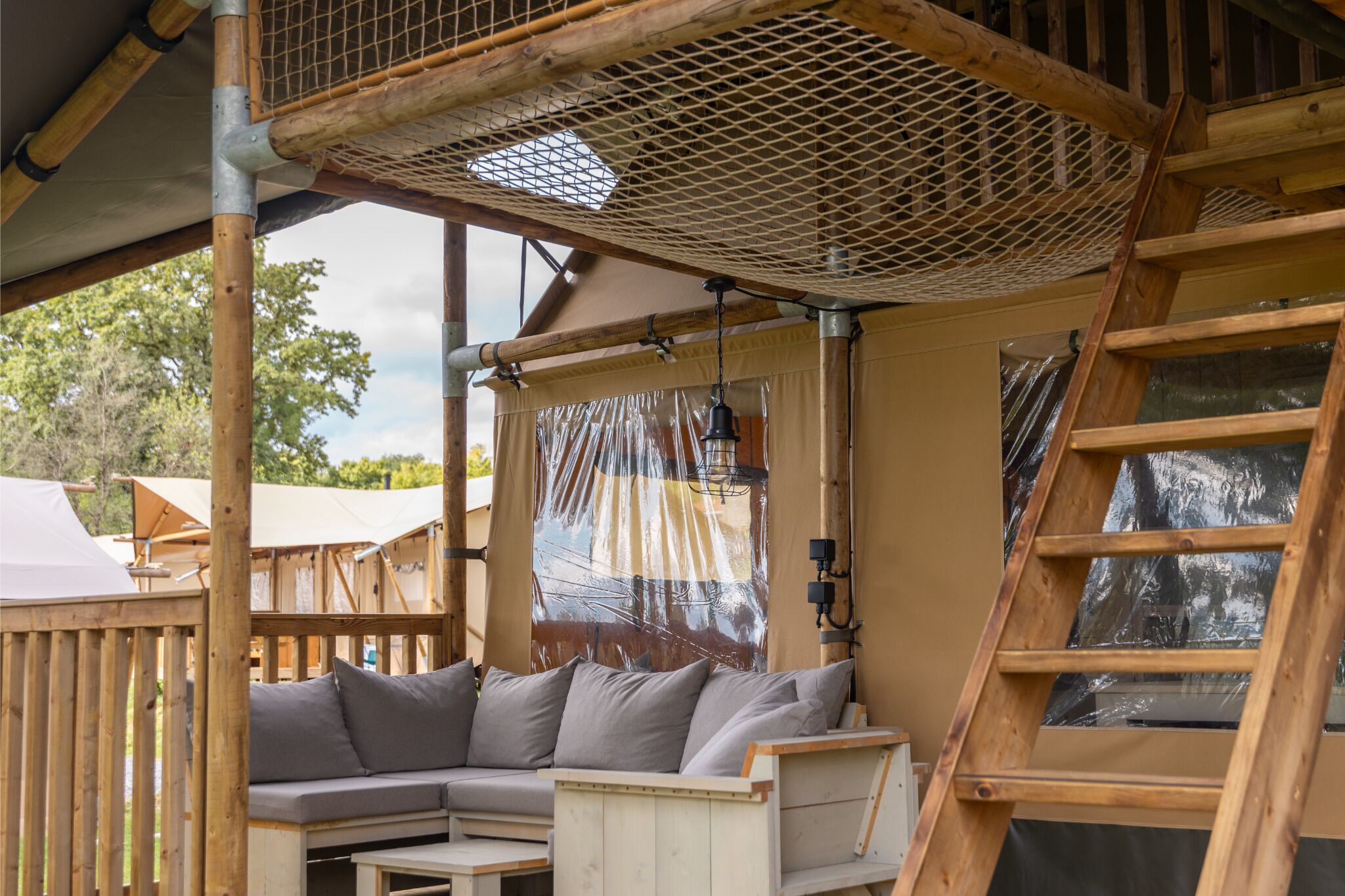 Una terraza de madera con zona de estar acolchada, una escalera y un techo de malla.