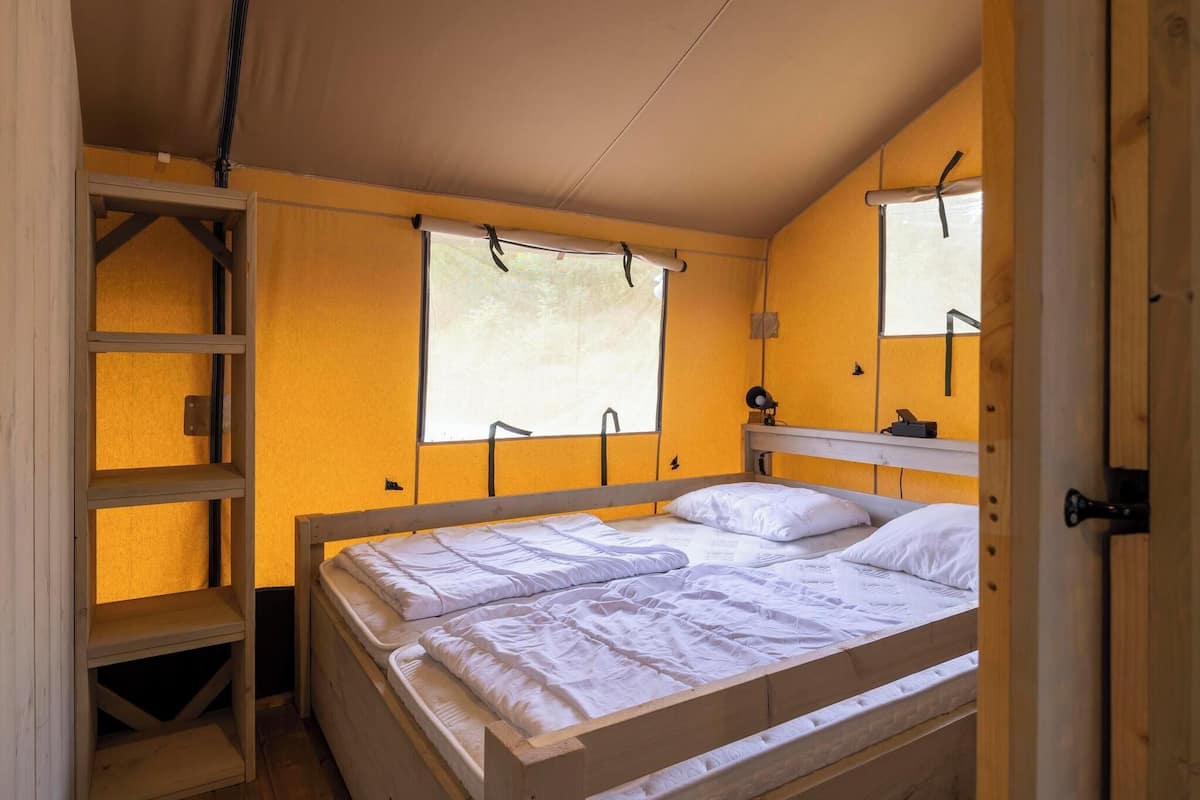 A single bed with white bedding in a room with yellow walls, a window, and a wooden shelf.
