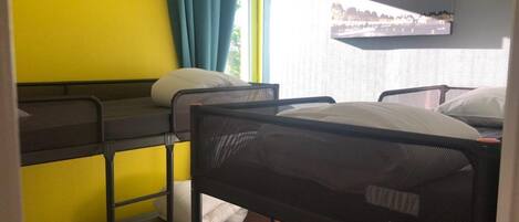 A dormitory room with bunk beds, a window with curtains, and a cityscape view on the wall.