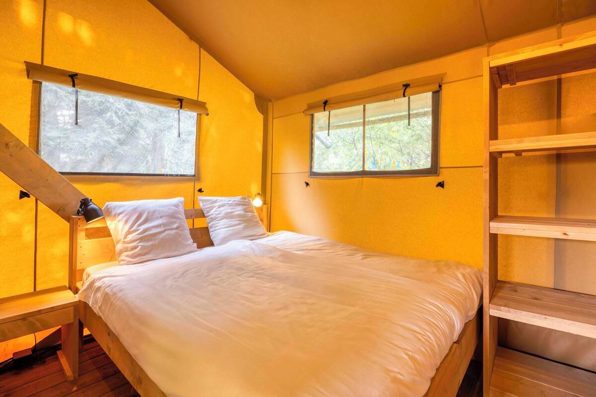 A bedroom with a wooden bed, two windows, and a wooden shelf unit.