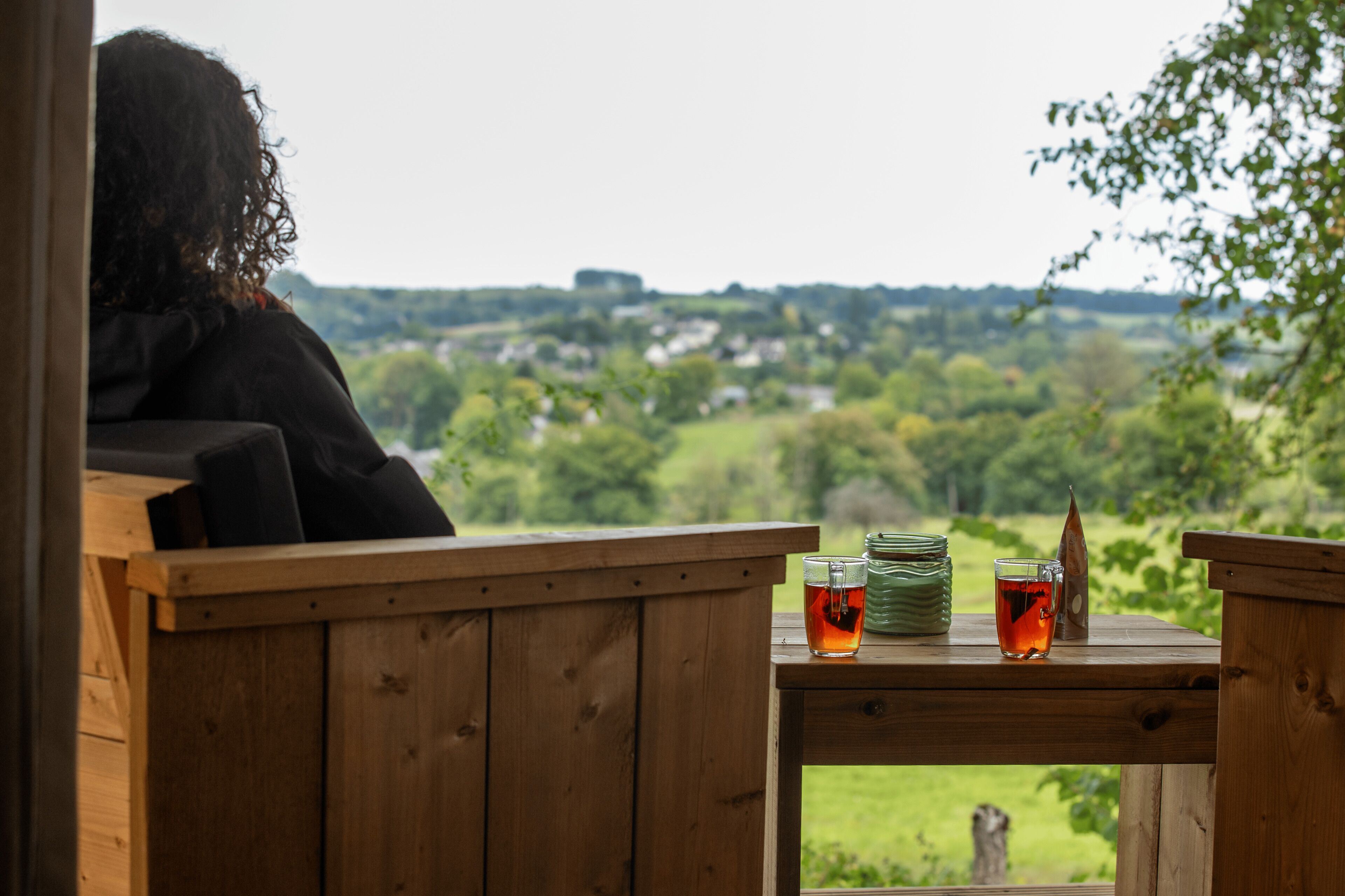 A wooden deck with a table, a glass of tea, and a stack of plates.