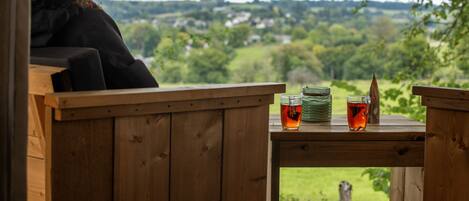 A wooden deck with a table, a glass of tea, and a stack of plates.