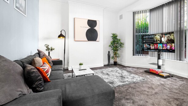 Una sala de estar moderna con un sofá gris, una mesa de centro, un televisor y un ventanal con persianas.