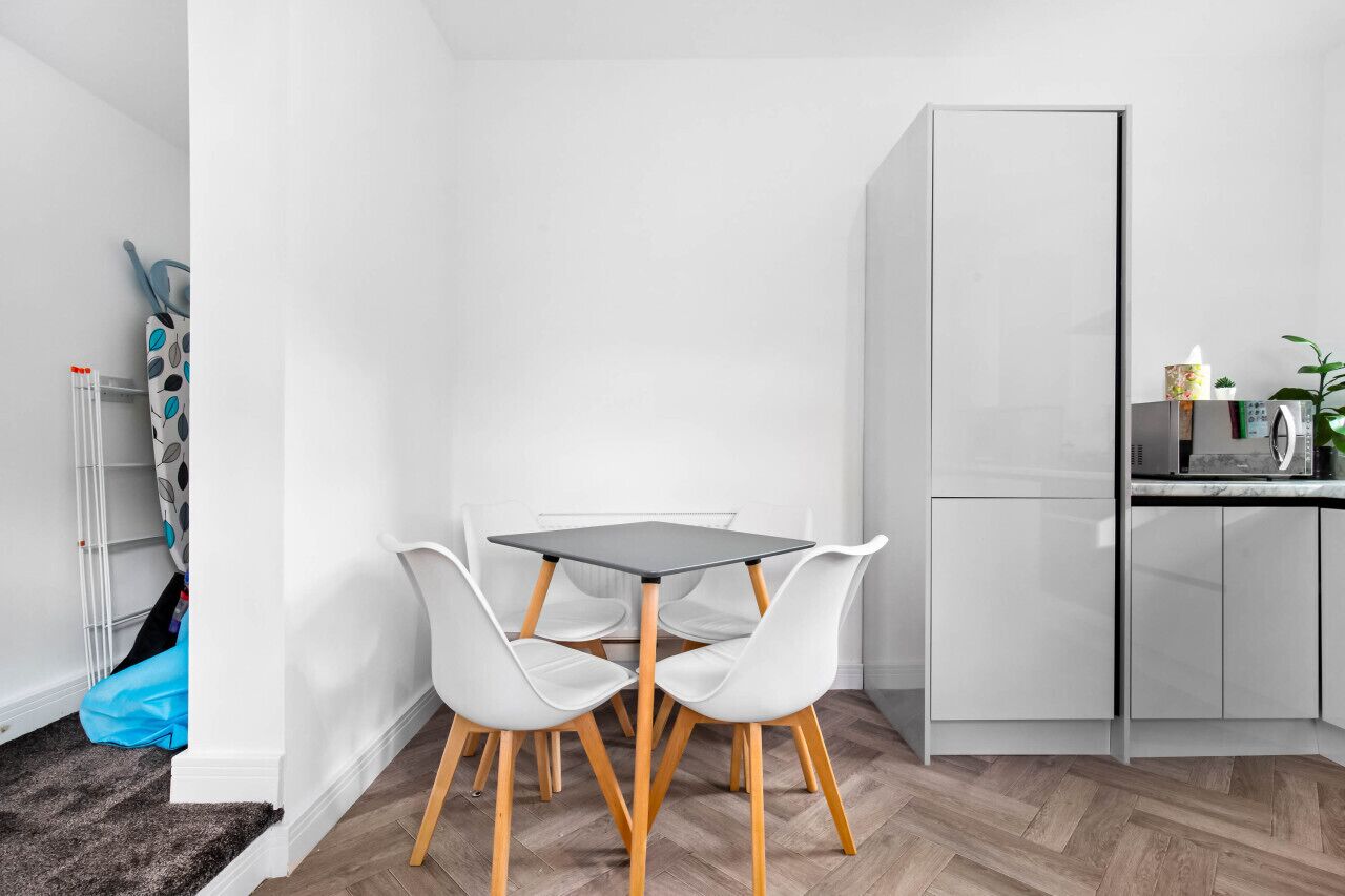 Une petite cuisine moderne avec des meubles blancs, un plan de travail noir et un coin repas comprenant des chaises blanches et une table noire.