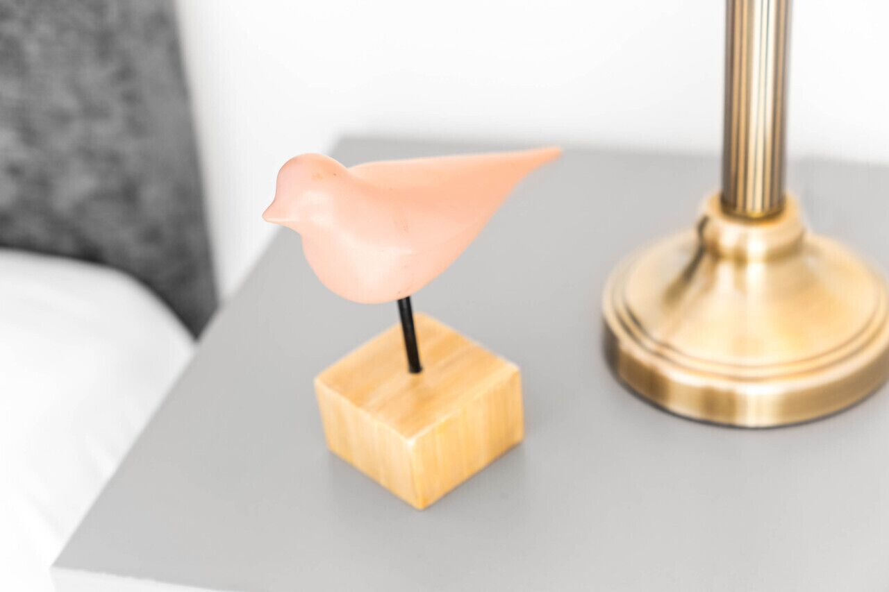 Ein Tisch mit einer dekorativen Vogelfigur auf Holzfuß und einer goldfarbenen Lampe daneben.