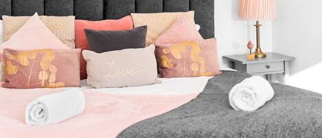 A neatly made bed with a variety of pillows and a rolled white towel.
