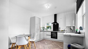 Una cocina moderna con armarios blancos, una campana extractora negra y un suelo de madera en patrón de espiga.