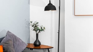 Una habitación con una mesa redonda de madera, una lámpara de pie negra y un florero con plantas verdes.