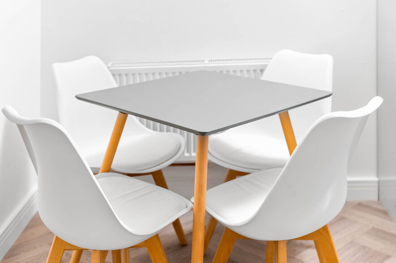 A modern dining area with a square table and four white chairs with wooden legs.