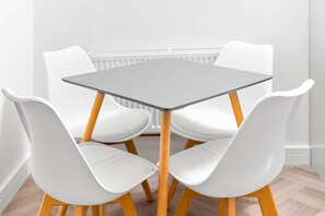 A modern dining area with a square table and four white chairs with wooden legs.