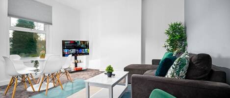Un salon moderne avec une table blanche, un canapé marron, des coussins verts et un téléviseur.