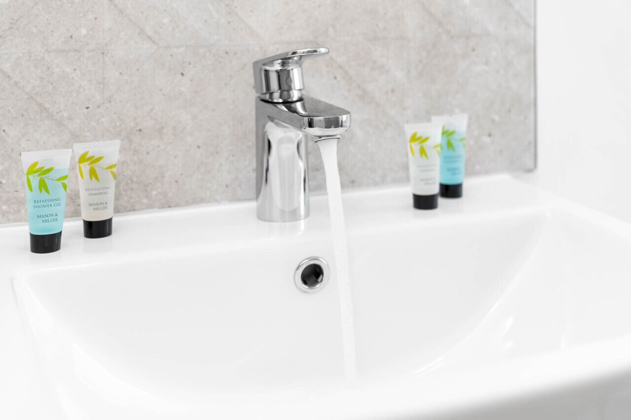 A bathroom sink with running water, three tubes of shampoo, and a modern faucet.