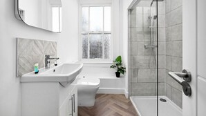 Een moderne badkamer met een grote spiegel, twee wastafels, een toilet, een douche en een raam met geëtste glas.