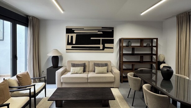 A modern living room with a sofa, coffee table, and chairs, a bookshelf, and a dining table.