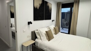 A modern bedroom with a large bed, a bedside table, a wall-mounted light, and a window with curtains.