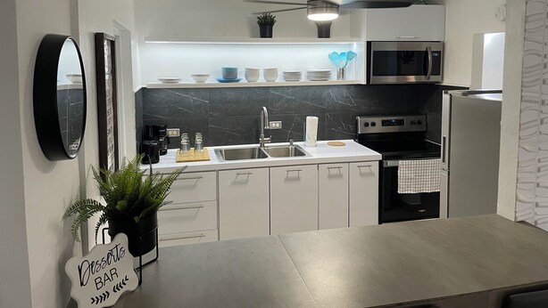 Una cocina moderna con armarios blancos, encimera negra, microondas, horno y ventilador de techo.