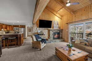 A spacious living area with a fireplace, wooden ceiling, and a large window overlooking a balcony. - ⭐️ LARGE DECK + FIREPLACE ⎮ Hot Tubs- Walk to Mtn ⎮ (Steamboat Springs)