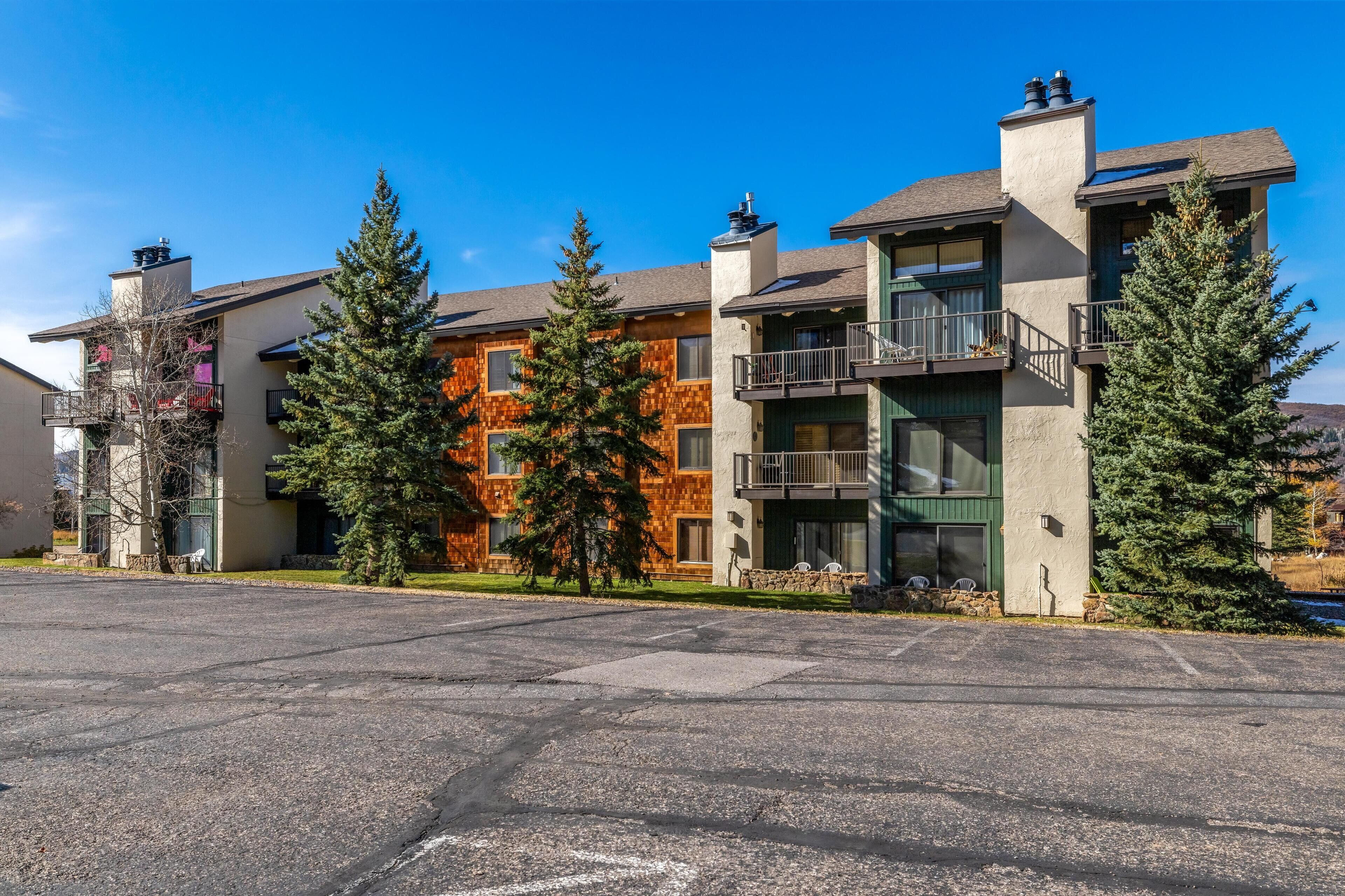 A row of modern multi-story buildings with balconies and large windows, surrounded by trees.