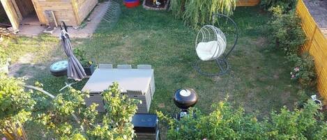 Un jardin avec un abri en bois, une chaise suspendue, une table et un barbecue.
