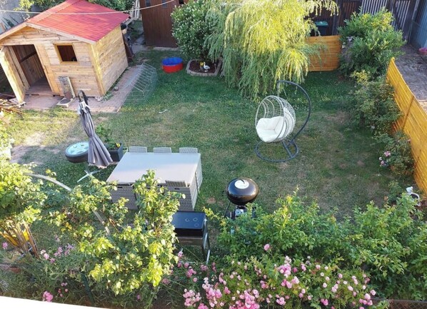 A backyard with a wooden shed, a hanging chair, a table, and a grill.