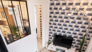 A modern living room with a grey sofa, a coffee table, a flat-screen TV, and a patterned wall. - Entire apartment - Saint-Dié-des-Vosges, France  (Saint-Dié-des-Vosges)