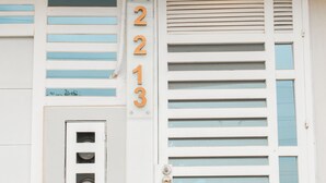 Fachada de un edificio con un acceso principal, el número '2213' encima de la puerta, y un sistema de ventilación con listones horizontales.