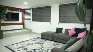 Una sala de estar con un sofá gris, un televisor grande montado en un panel de madera y una alfombra estampada.