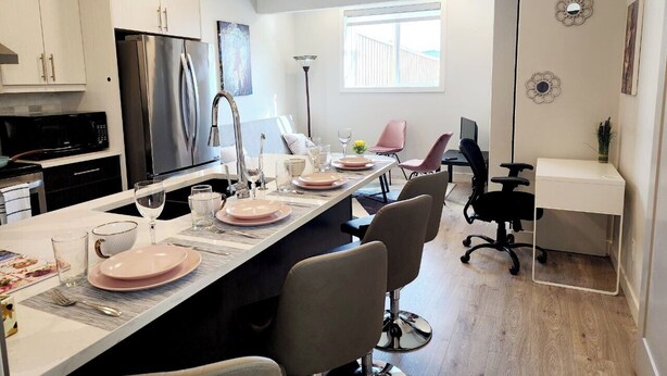 Una cocina moderna con armarios blancos, un refrigerador de acero inoxidable y un comedor con una mesa larga dispuesta para cuatro personas.