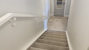 Una escalera alfombrada con paredes blancas y una puerta al final.