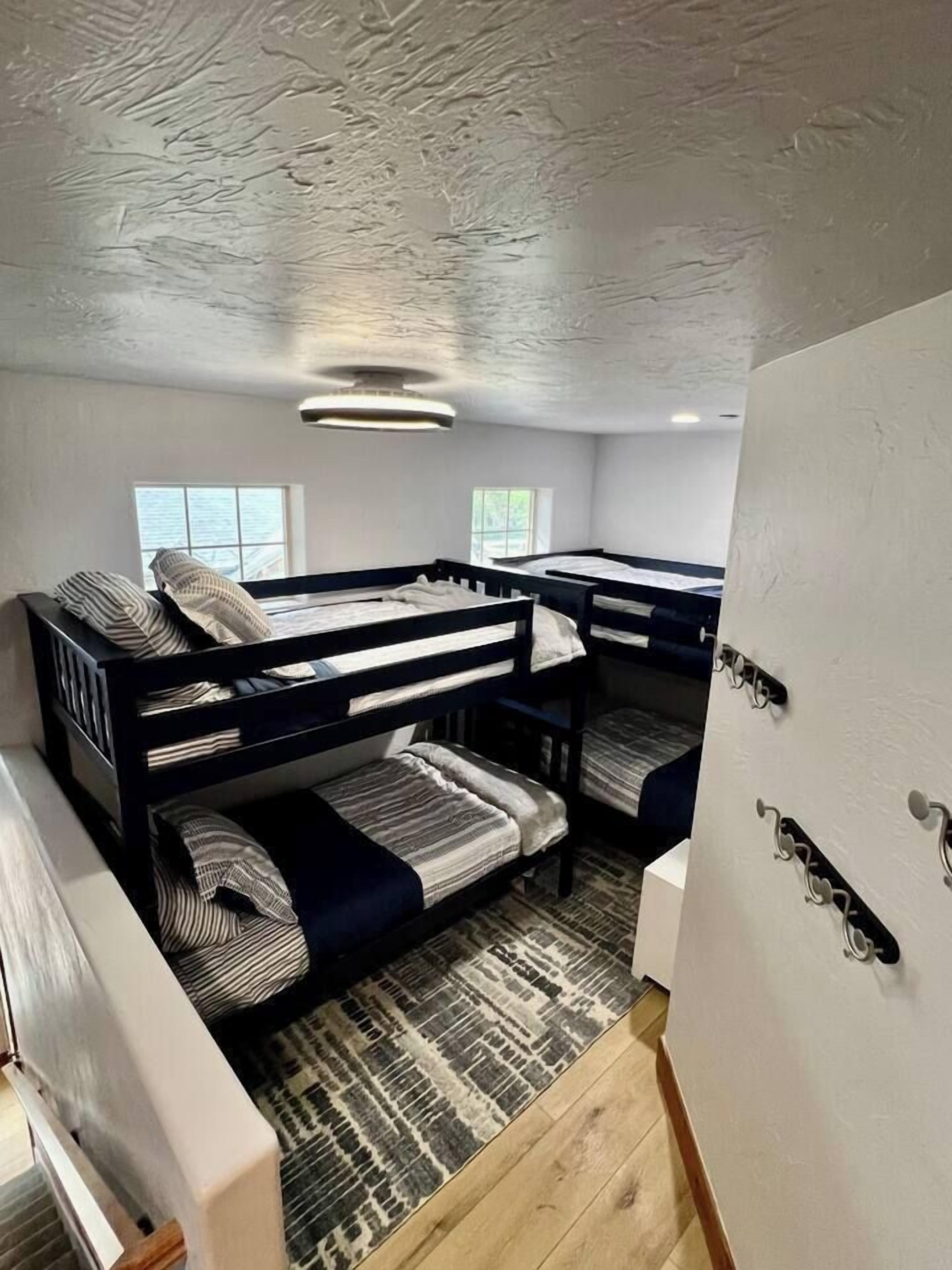 Une chambre avec un lit superposé, un tapis à motifs, un luminaire au plafond et une fenêtre.