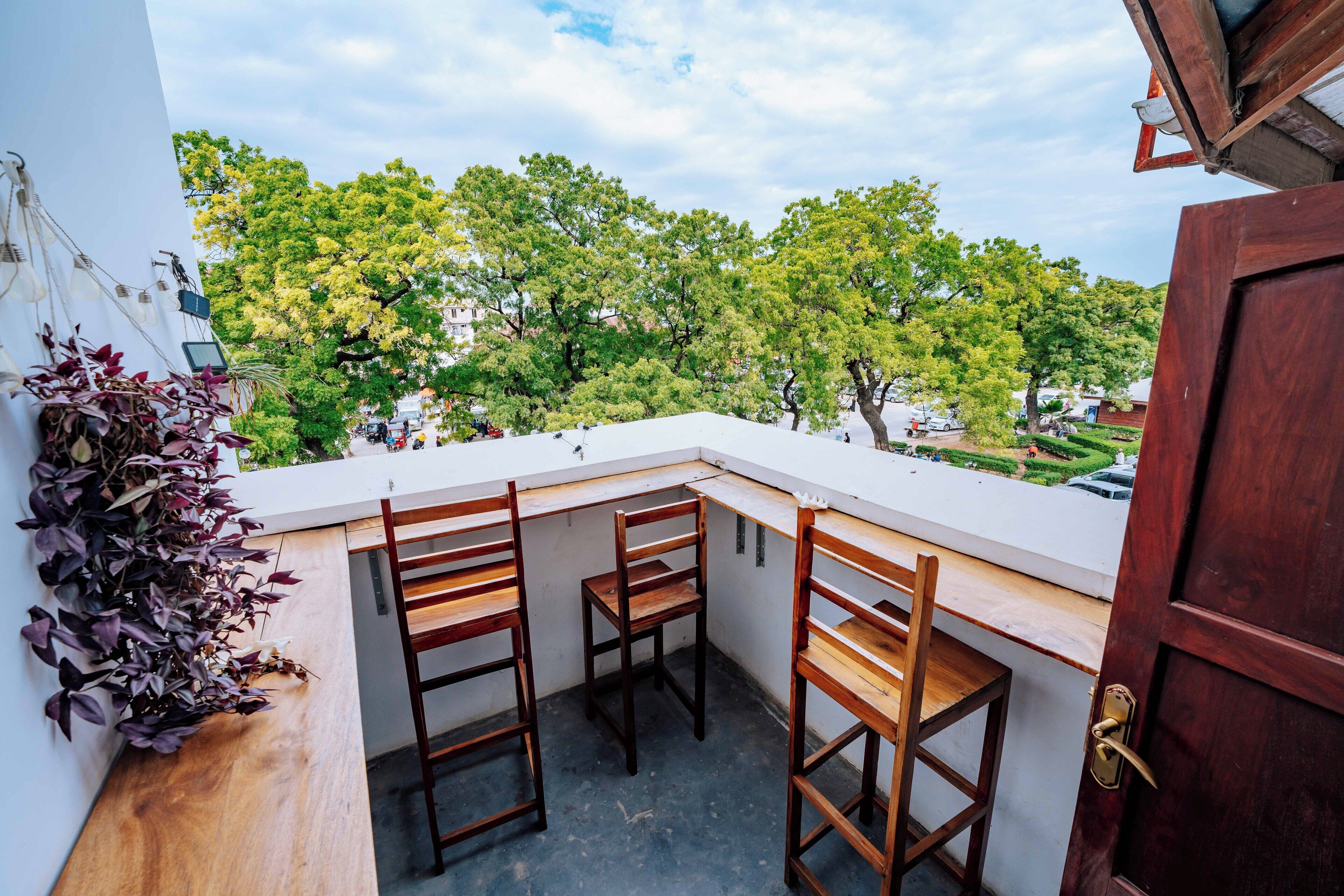 A balcony with three wooden chairs and a potted plant.