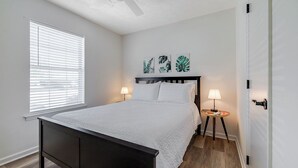 A bedroom with a bed, bedside lamps, a window with blinds, and a door.
