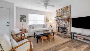 A living room with a stone fireplace, white sofa, wooden coffee table, and a flat-screen TV.