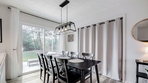 A dining area with a black table and chairs, a pendant light, and a view of the outdoors through large windows.