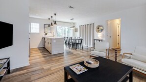 A modern living room with a black coffee table, a white sofa, and a dining area with a kitchen in the background.