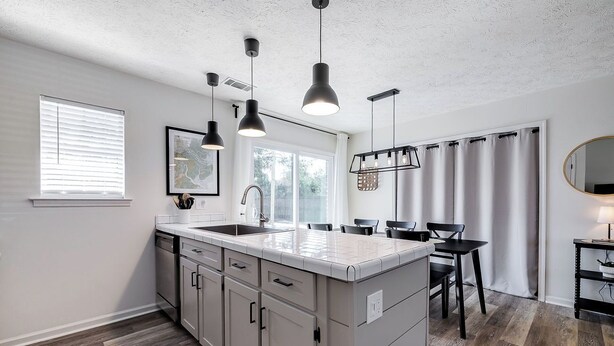 A modern kitchen with a central island, pendant lights, and a dining area with a table and chairs.