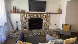 A living room with a stone fireplace, a mounted TV, and a sofa with cushions.