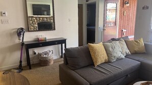 A living room with a grey sofa, a console table, a vacuum cleaner, and a stone fireplace.