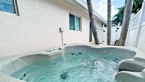 A hot tub with a stone exterior, surrounded by a white fence and palm trees.
