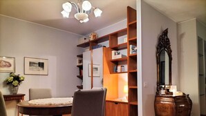 Un comedor con una mesa redonda, dos sillas, una araña, una estantería y un espejo.