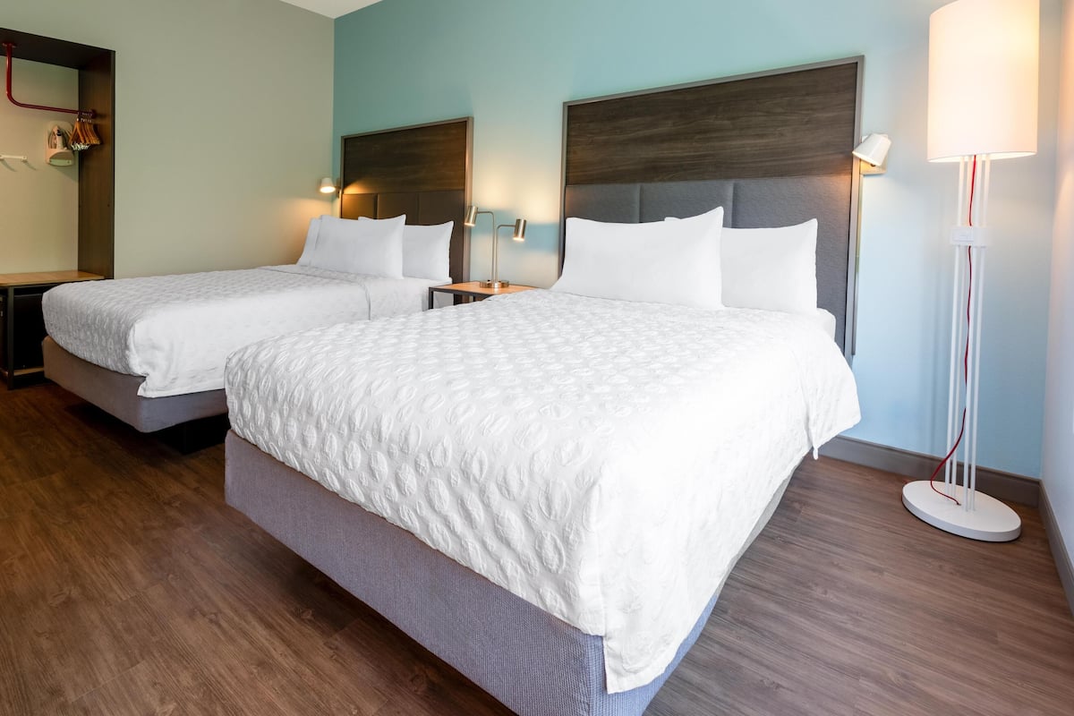A hotel room with two beds, wooden flooring, and a modern design.