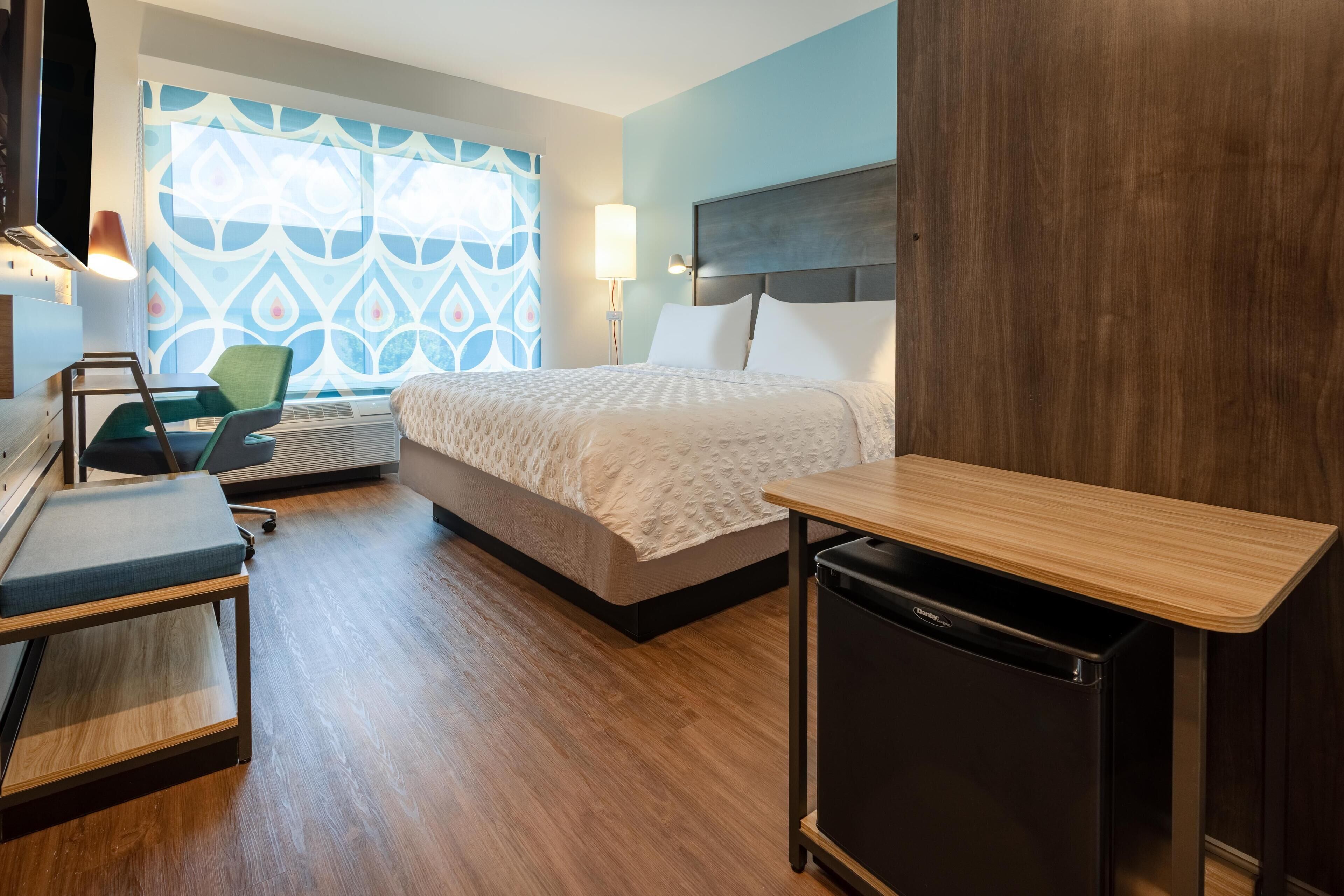 Une chambre d’hôtel équipée d’un lit, d’une table de chevet, d’un bureau, d’une chaise et d’un petit réfrigérateur.