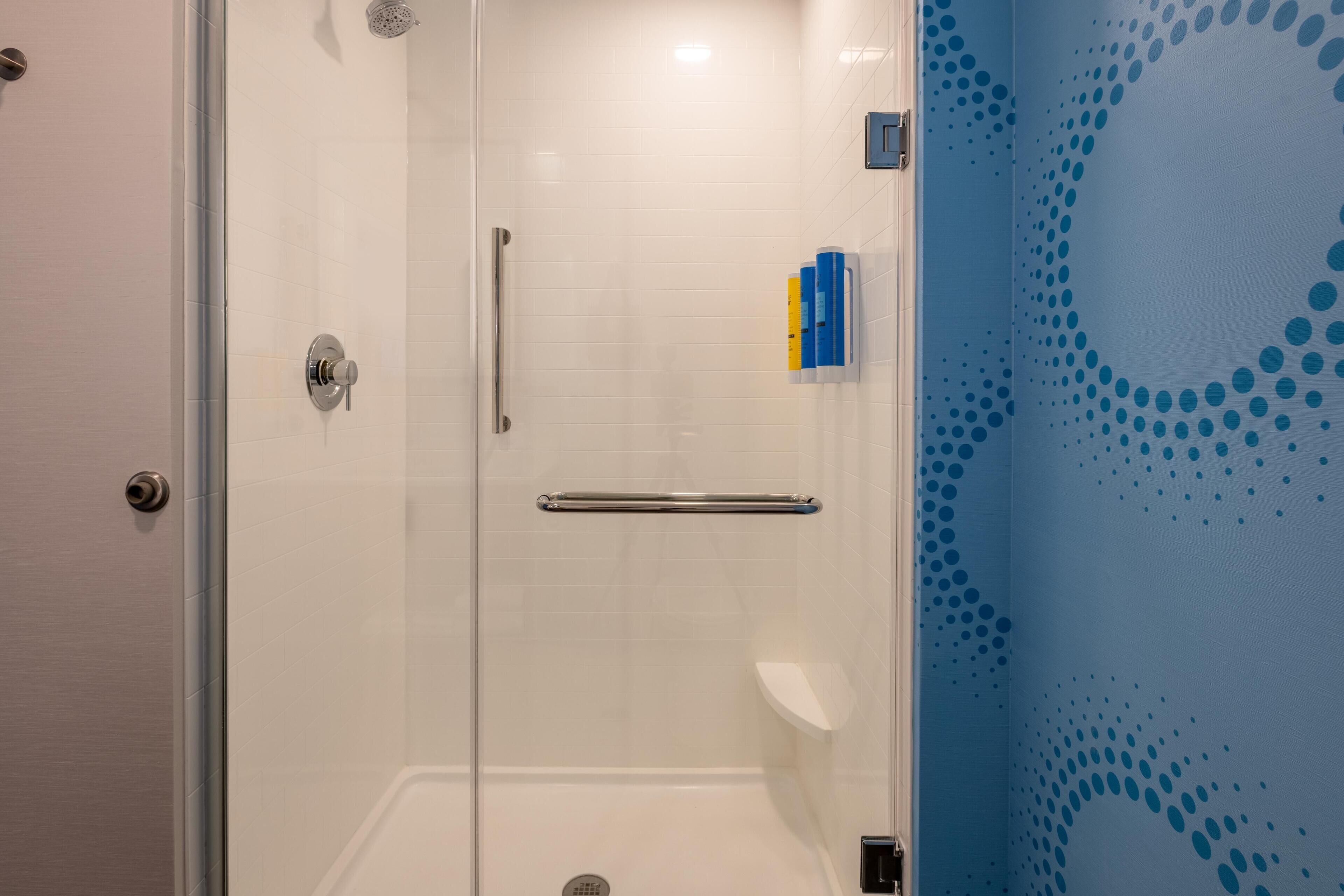 Une douche fermée par des parois en verre, dotée d’une barre d’appui, d’un mur recouvert de carreaux blancs et d’un mur bleu orné d’un motif à pois.