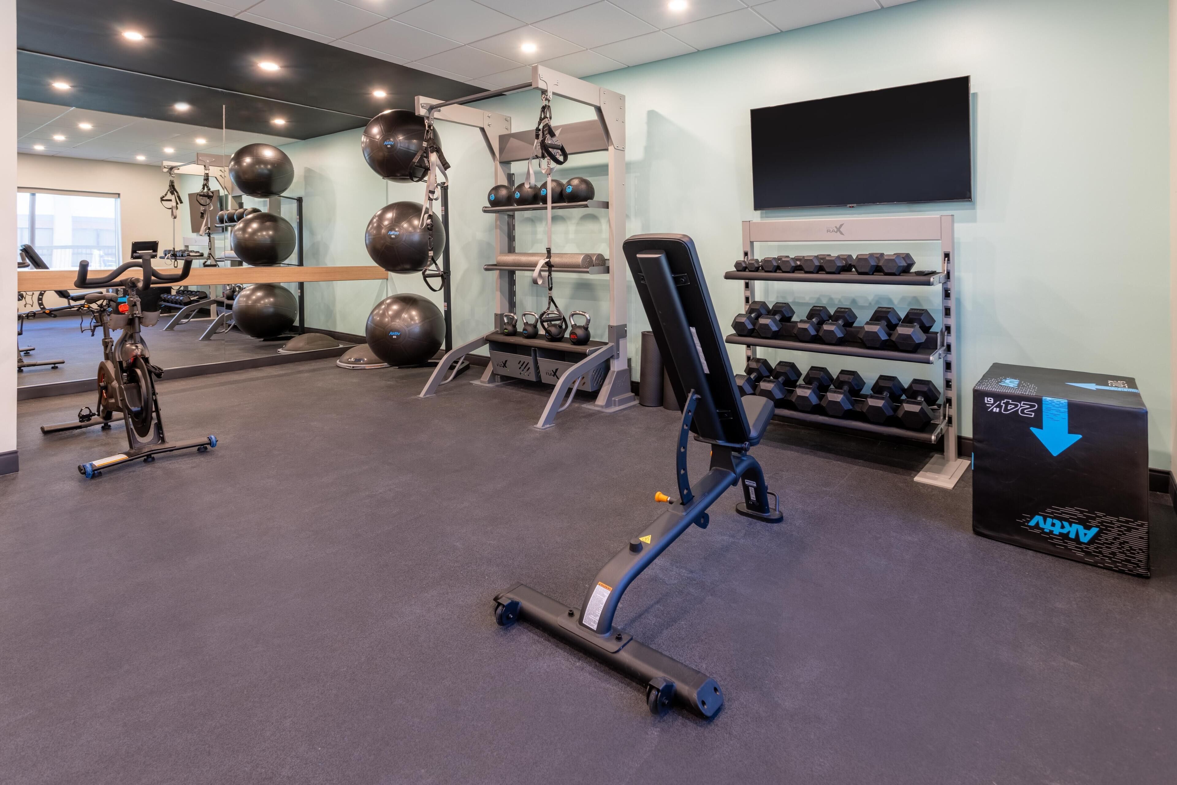 Un gimnasio con equipo de ejercicio, un espejo y un televisor en la pared.