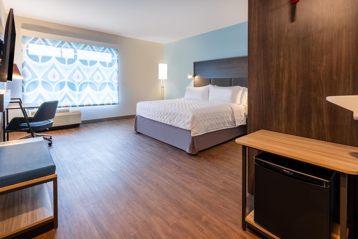 A hotel room with a bed, a desk, a chair, a lamp, and a small refrigerator.