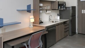 A modern kitchen with a built-in dishwasher, a microwave, and a stainless steel refrigerator. There is a wooden countertop and a chair with a mesh backrest. - Home2 Suites By Hilton Lima (Lima)