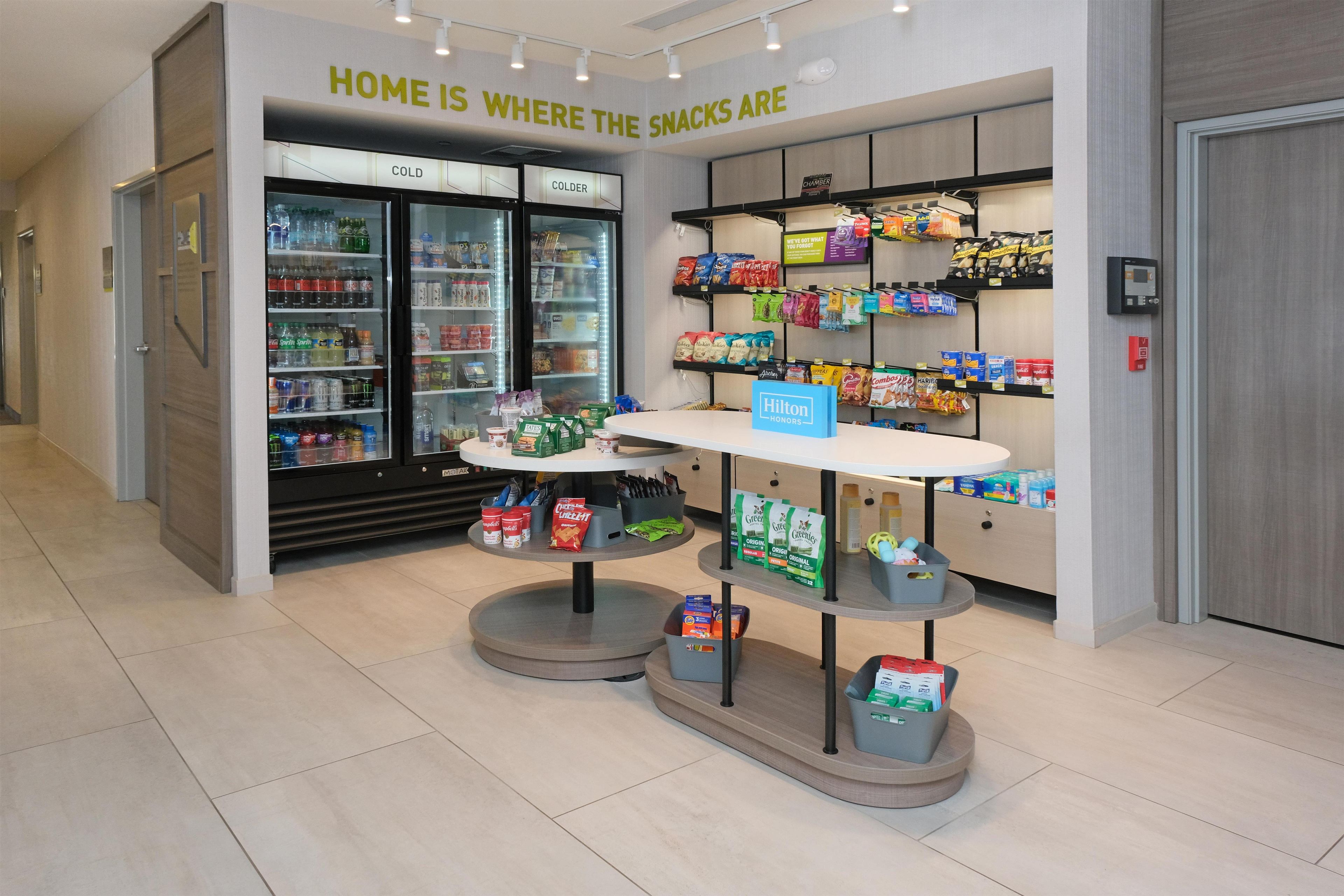 Un quiosco de snacks con un cartel que dice 'HOME IS WHERE THE SNACKS ARE' y una variedad de bocadillos exhibidos en estantes.