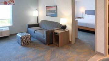 Une chambre d’hôtel avec un canapé, un tapis à motifs, une table de chevet avec une lampe, un lit et une fenêtre donnant sur un paysage.