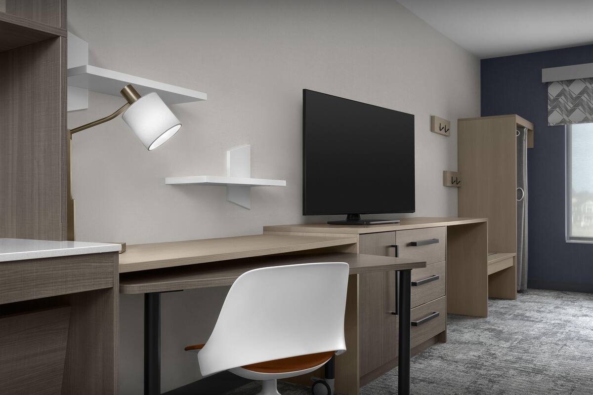 Un dormitorio moderno con escritorio, silla, televisor y armario.