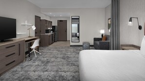 Een moderne hotelkamer met een groot bed, een bureau met stoel, een televisie en een kitchenette op de achtergrond.